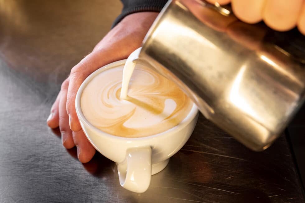 A warm glass of café con leche with steamed milk swirling into dark coffee